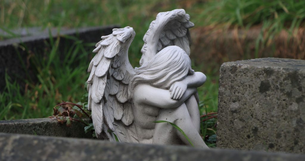 A tranquil angel statue resting in a lush, grassy cemetery conveying peace and serenity.